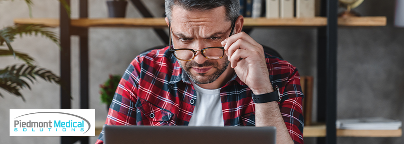 A man lowering his glasses while looking at a laptop 