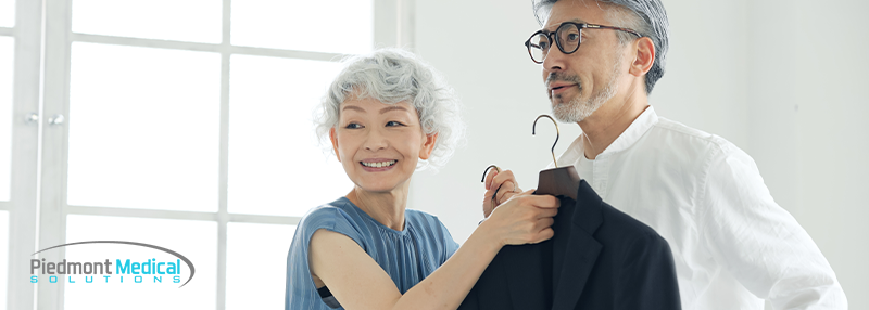 Elderly couple; wife holding up a dress coat against husband smiling