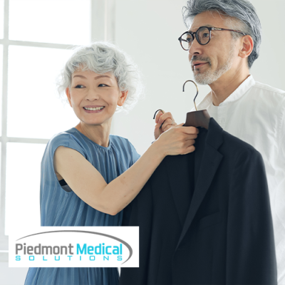 Elderly couple; wife holding up a dress coat against husband smiling