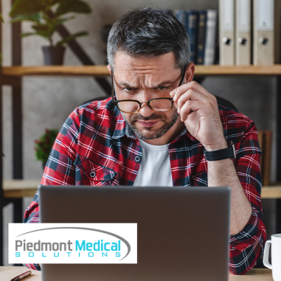 A man lowering his glasses while looking at a laptop 