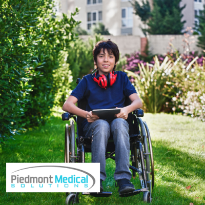 Boy in wheelchair outside smiling with headphones around his neck and tablet in his hands 